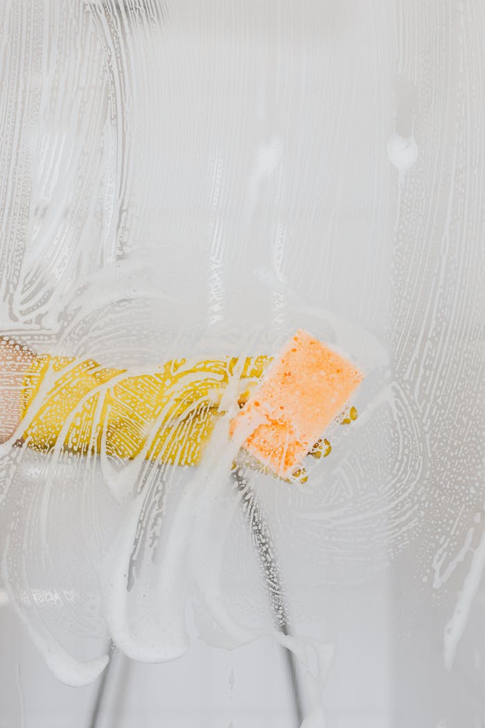 services-04 A gloved hand cleans glass with a sponge and soapy water, ensuring hygiene.