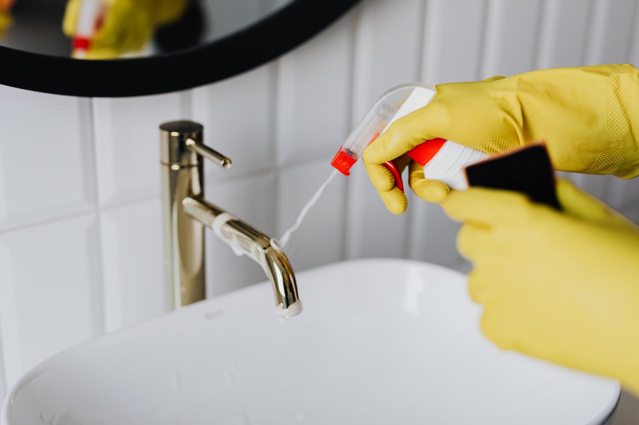 team-04 From above anonymous housekeeper in yellow rubber gloves spraying cleaner to chrome water faucet in bathroom